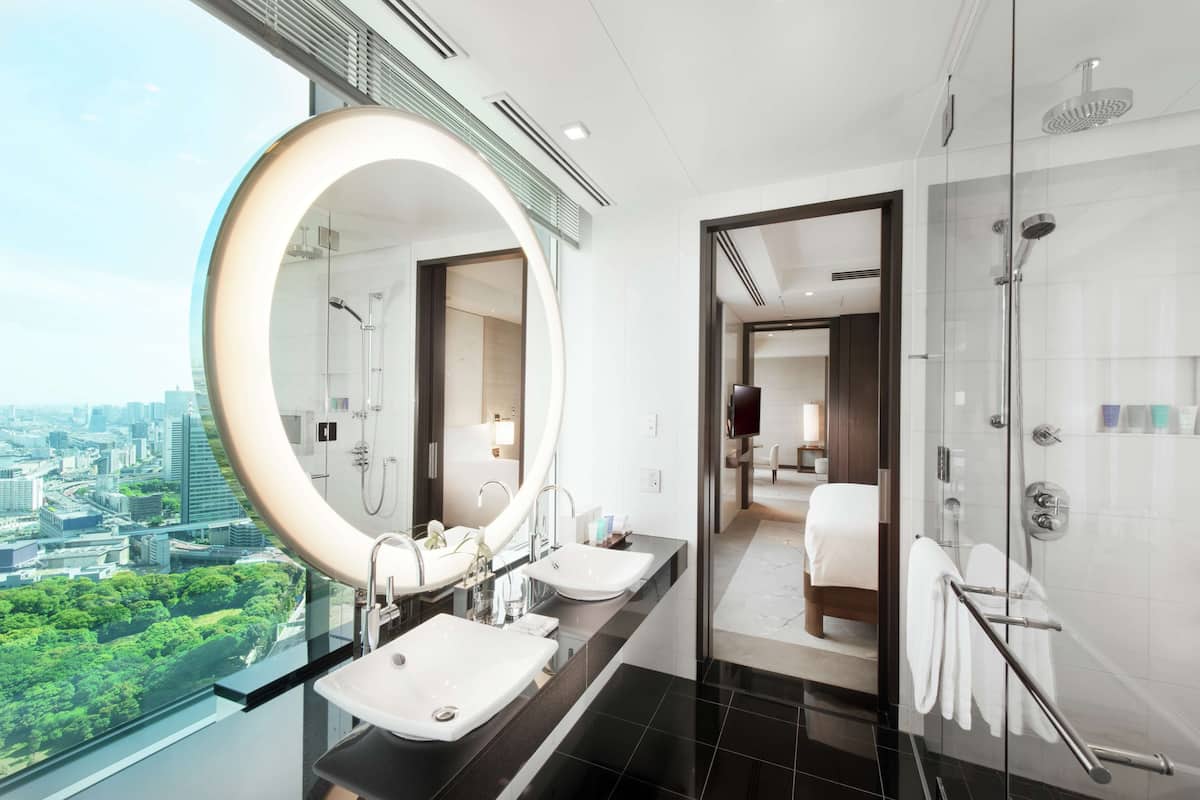 Un baño moderno con un espejo grande, dos lavamanos, una ducha y vistas de la ciudad.