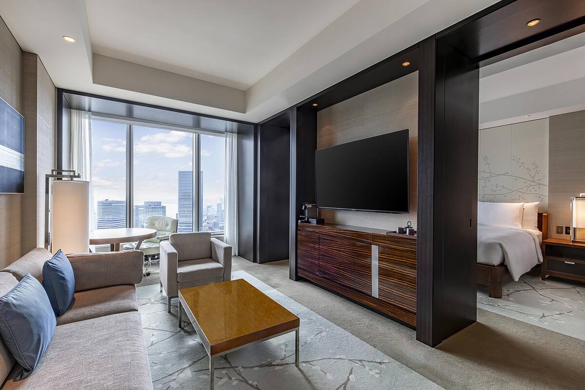 A modern hotel room with a large TV, a sofa, a coffee table, a desk, and a bed.
