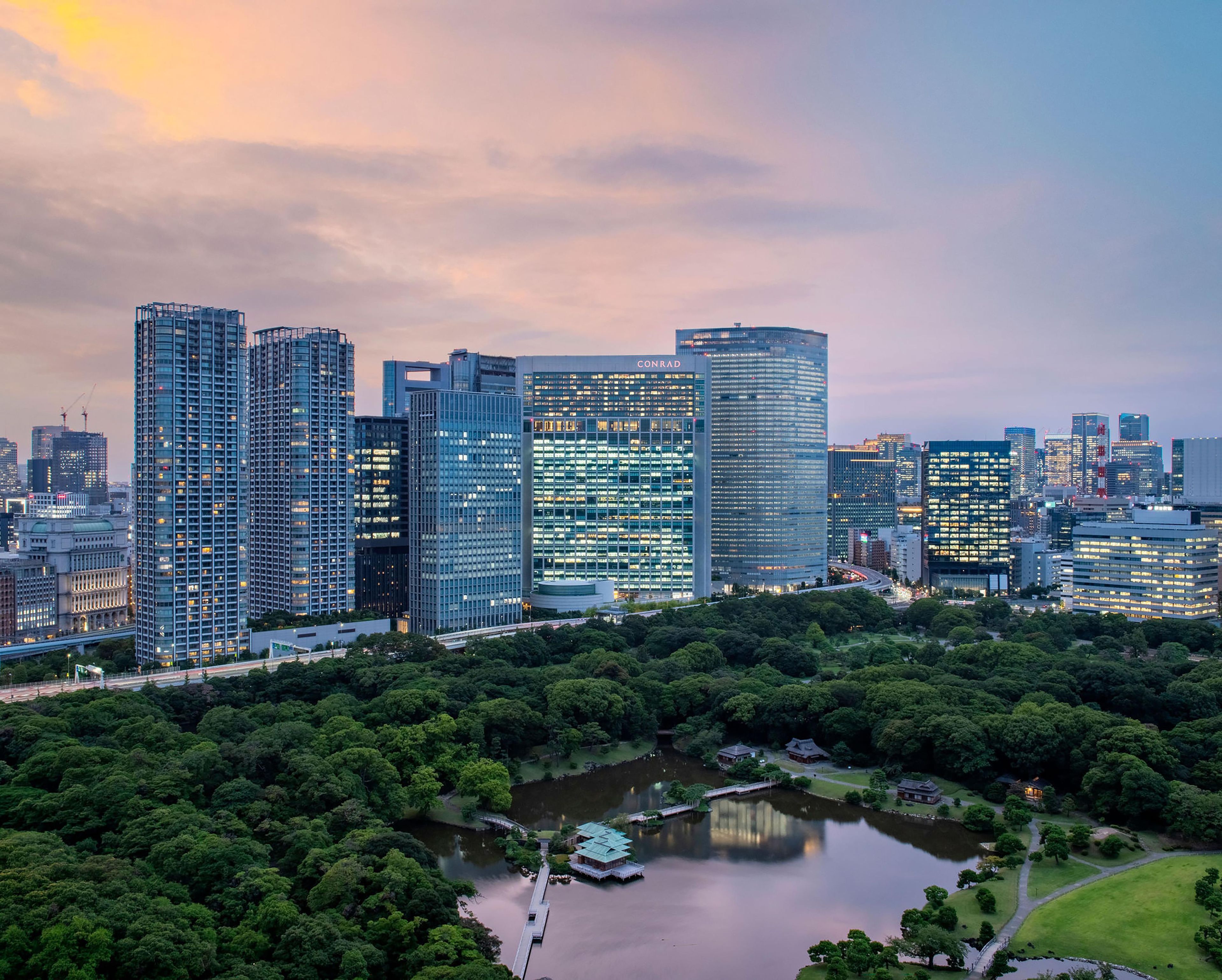 A cityscape with modern high-rise buildings, a park with a lake, and a traditional building with a green roof.