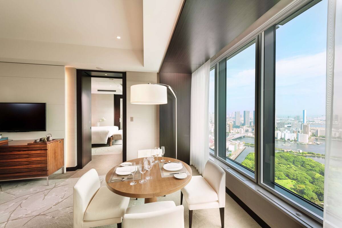 Habitación de hotel moderna con zona de comedor, televisor de pantalla plana y vistas a la ciudad.