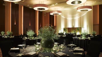 Una sala da pranzo formale con tavoli rotondi, lampadari eleganti e un grande centrotavola decorativo.