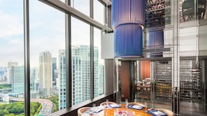 A dining area with a large round table, chairs, and a city view through large windows. - Conrad Tokyo (Tokyo)