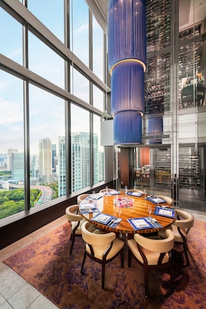 A dining area with a large round table, chairs, and a city view through large windows. - Conrad Tokyo (Tokyo)