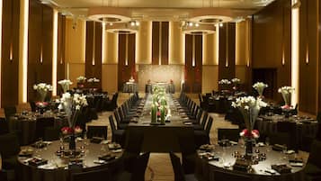 Un amplio salón de banquetes con largas mesas dispuestas para cenar, con centros de mesa florales e iluminación moderna.