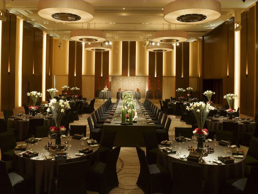 Un amplio salón de banquetes con largas mesas dispuestas para cenar, con centros de mesa florales e iluminación moderna.