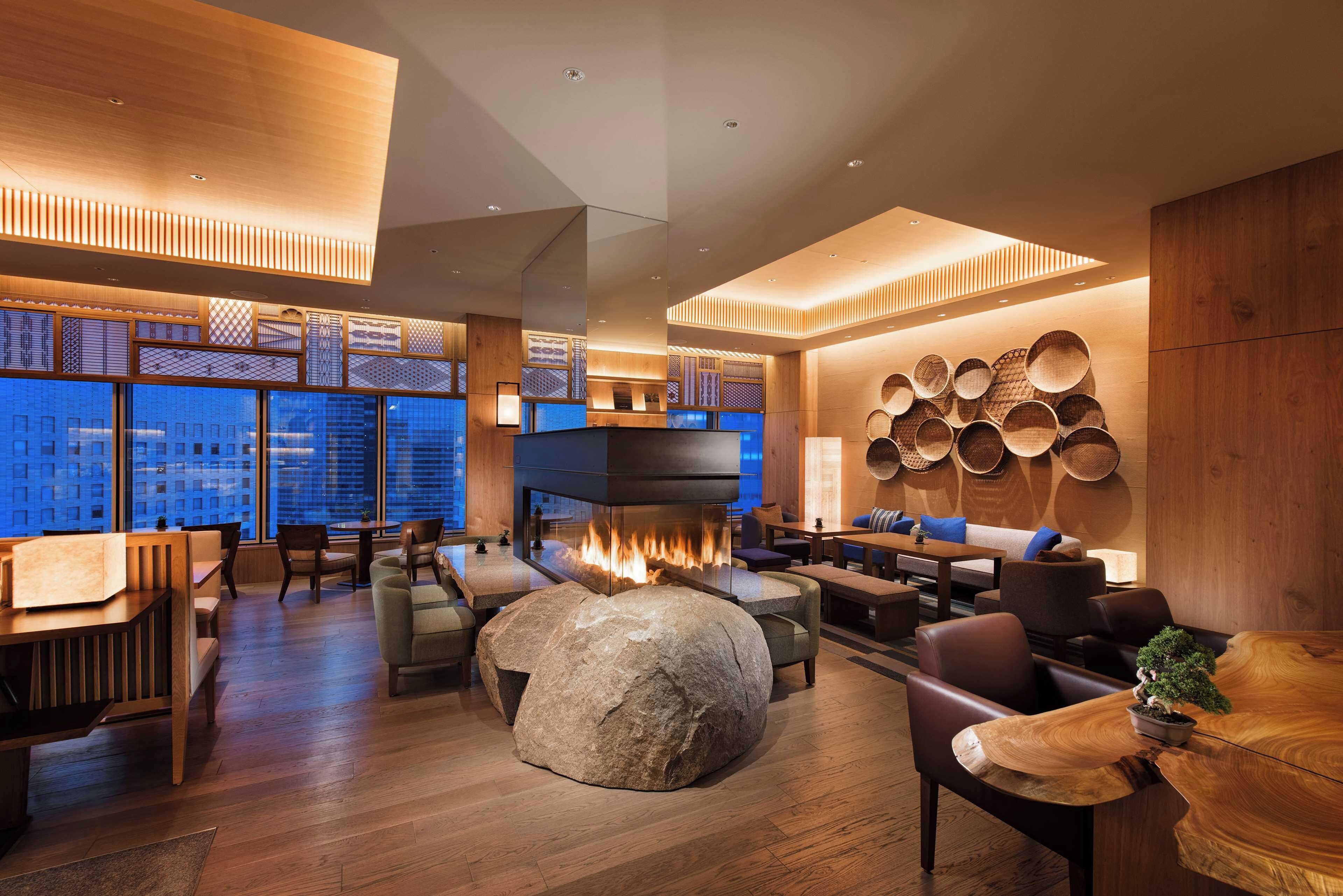 A modern interior with a stone fireplace, wooden furniture, and a view of the cityscape through large windows.