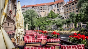Outdoor seating with red and white checkered cushions, a river view, and historic buildings in the background. - Hotel Dvorak (Cesky Krumlov)