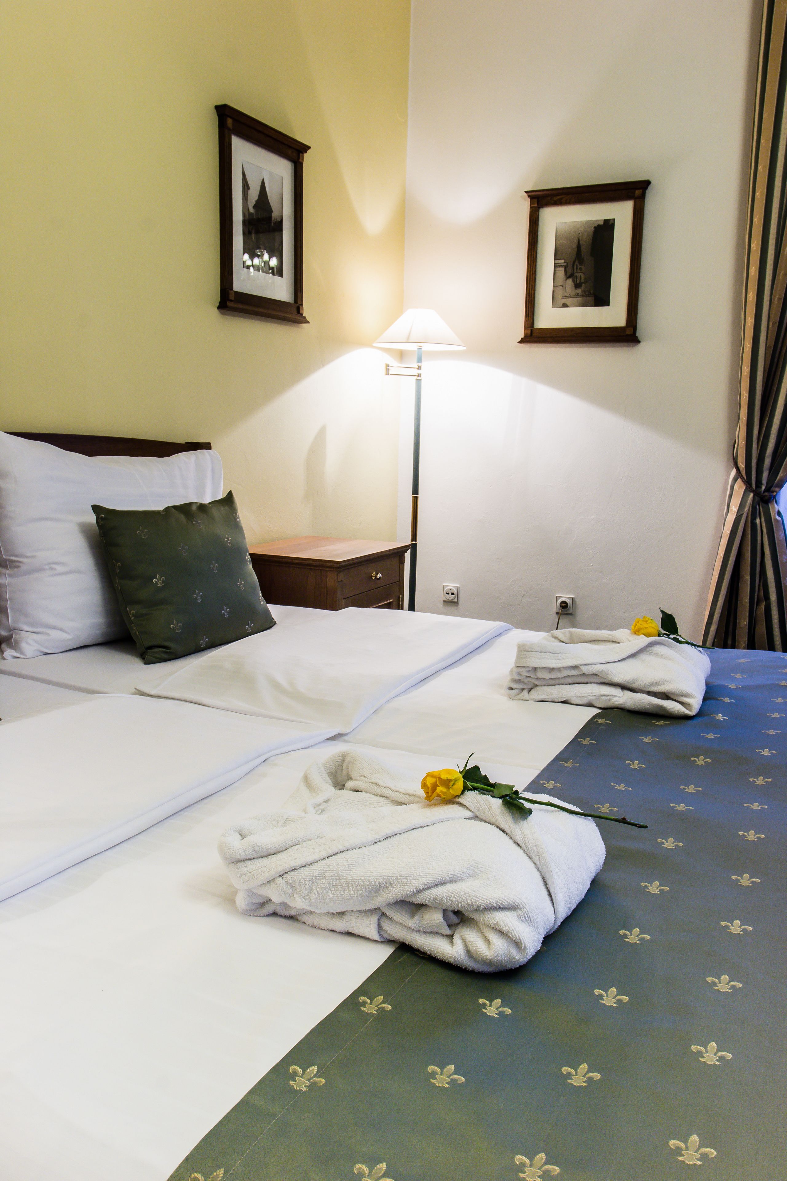 Een hotelkamer met twee bedden, elk voorzien van netjes opgevouwen handdoeken en een roos. Er hangen ingelijste foto’s aan de muur en een lamp op een nachtkastje.