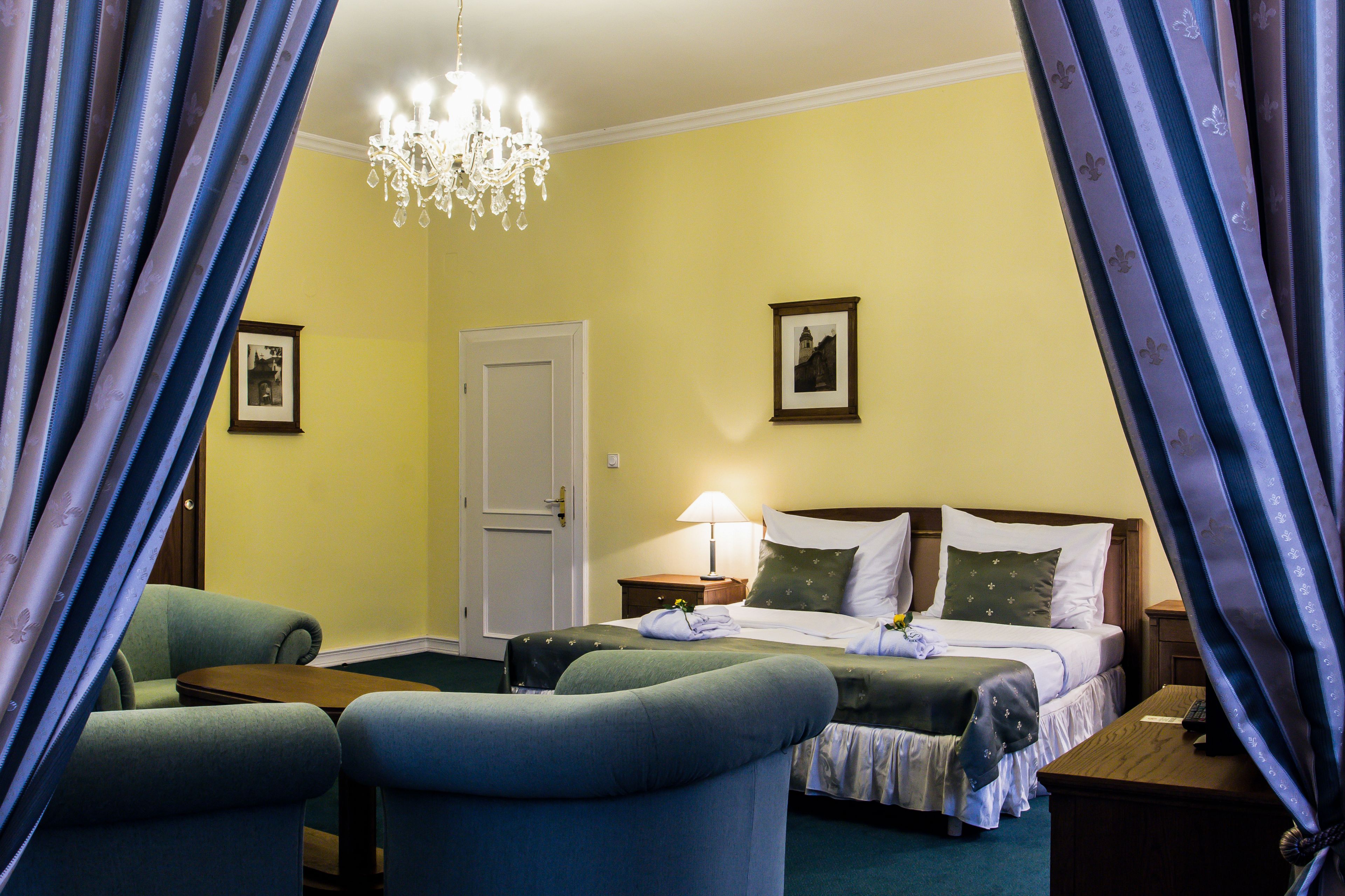 Una habitación de hotel con una cama, dos sillones, una mesita de noche con lámpara y un candelabro.