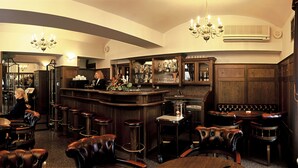 A bar area with leather seating, a bar counter, and a chandelier. - Hotel Dvorak (Cesky Krumlov)