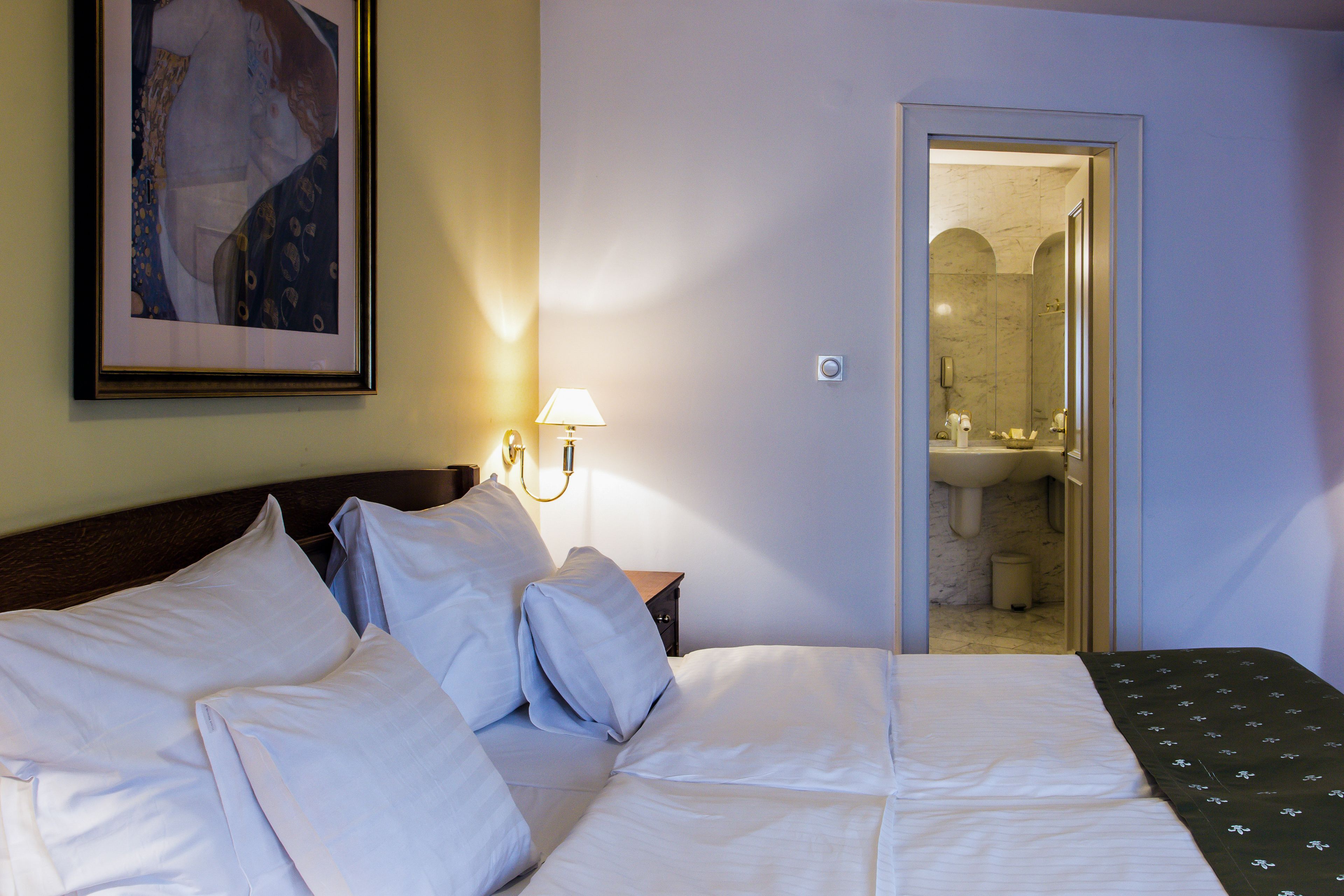 Habitación de hotel con una cama bien hecha, una mesita de noche con lámpara y un cuadro en la pared.