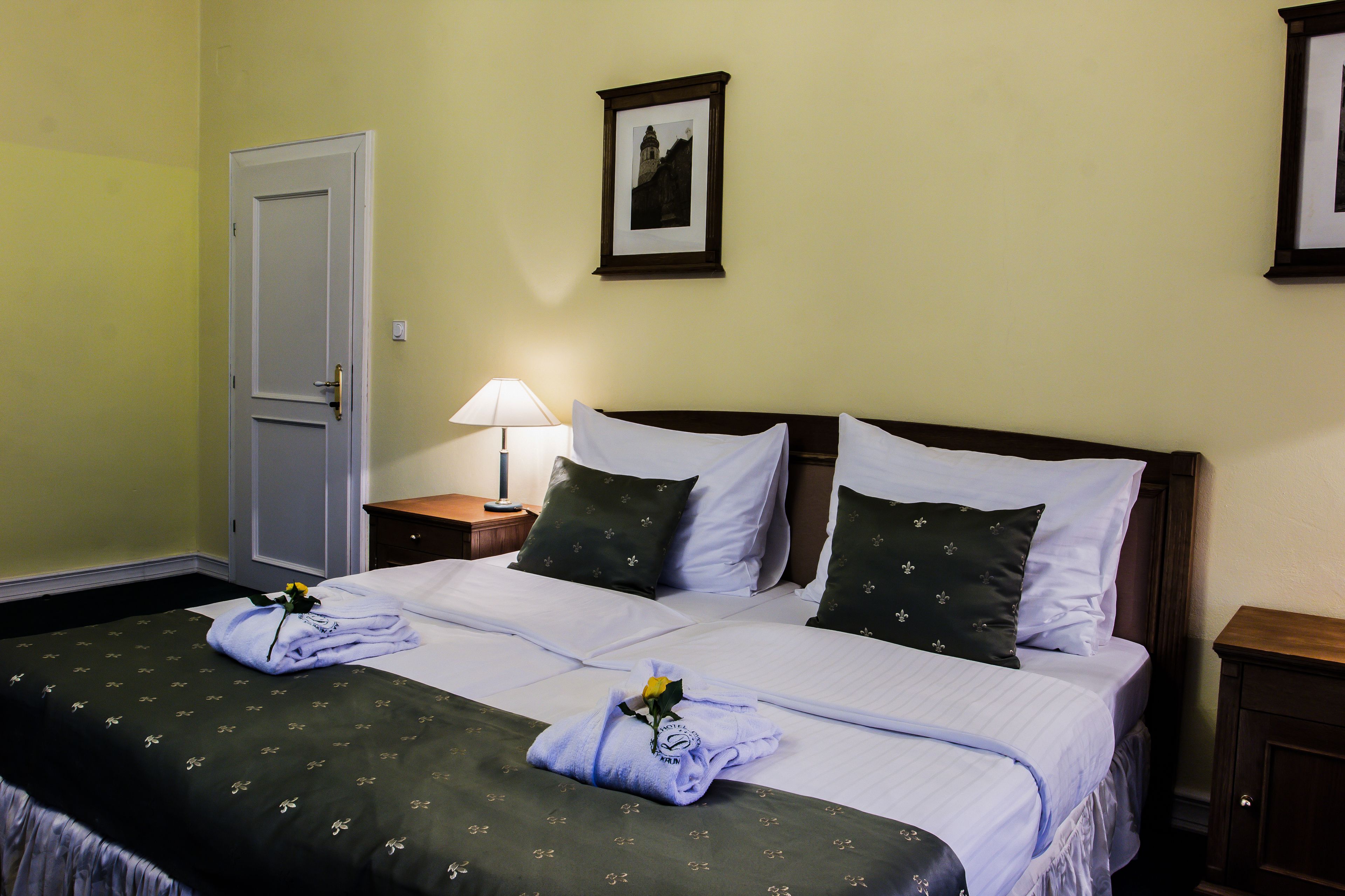 A hotel room with a double bed, two pillows, a bedside table with a lamp, and a framed picture on the wall.