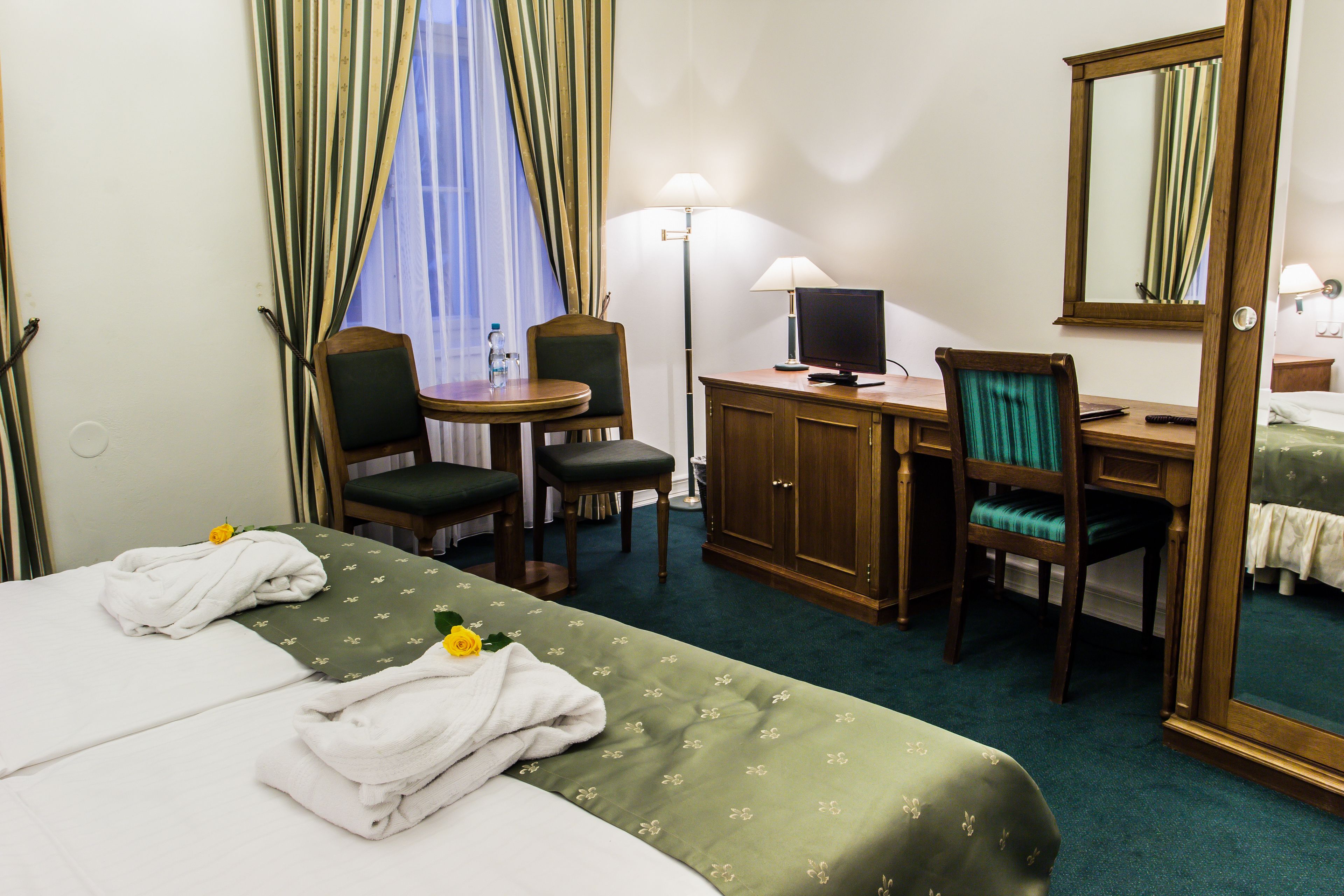 Una habitación de hotel con cama, escritorio, computadora, silla, lámpara y espejo.