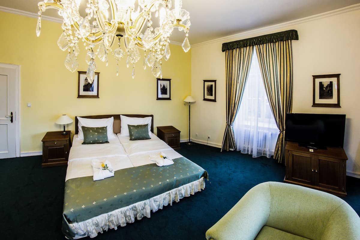 A hotel room with a large bed, a television, a chandelier, and a window with curtains.