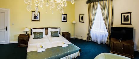 A hotel room with a large bed, a television, a chandelier, and a window with curtains.