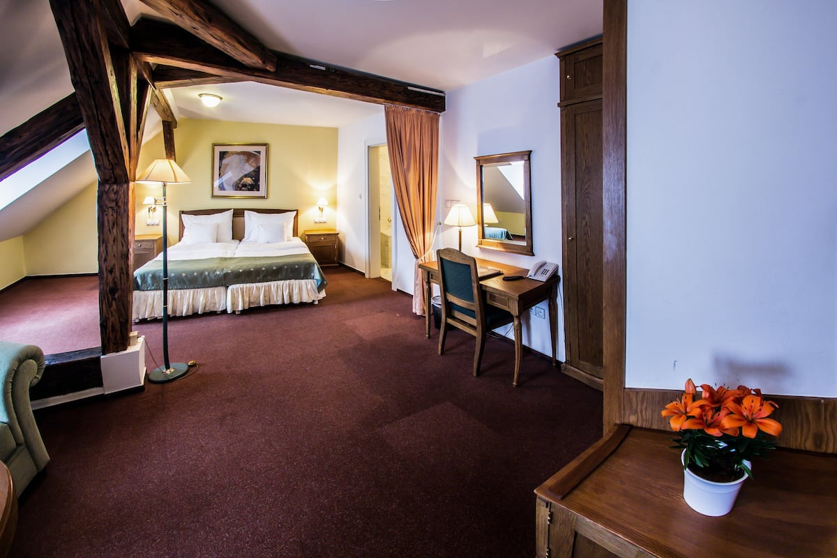 A hotel room with a bed, desk, chair, and a potted plant.