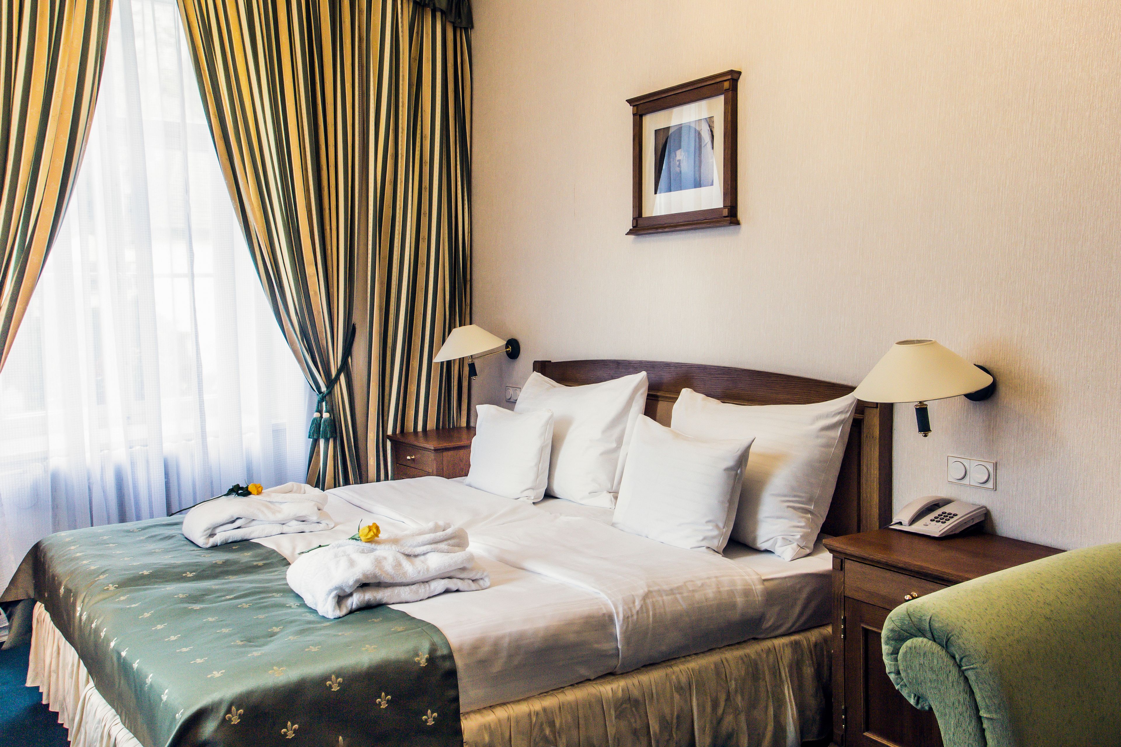 Una habitación de hotel con una cama, dos lámparas de noche, un teléfono y un cuadro en la pared.