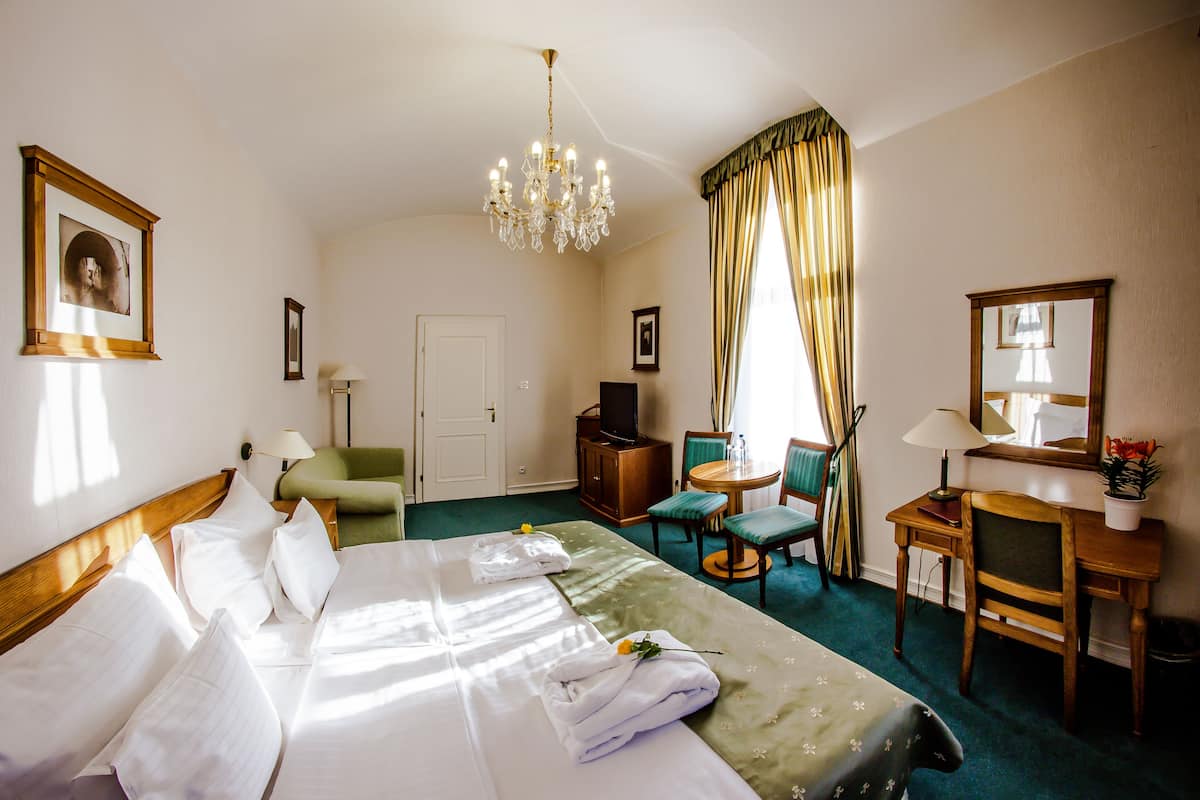 A hotel room with a bed, a desk, a chair, a television, and a chandelier.