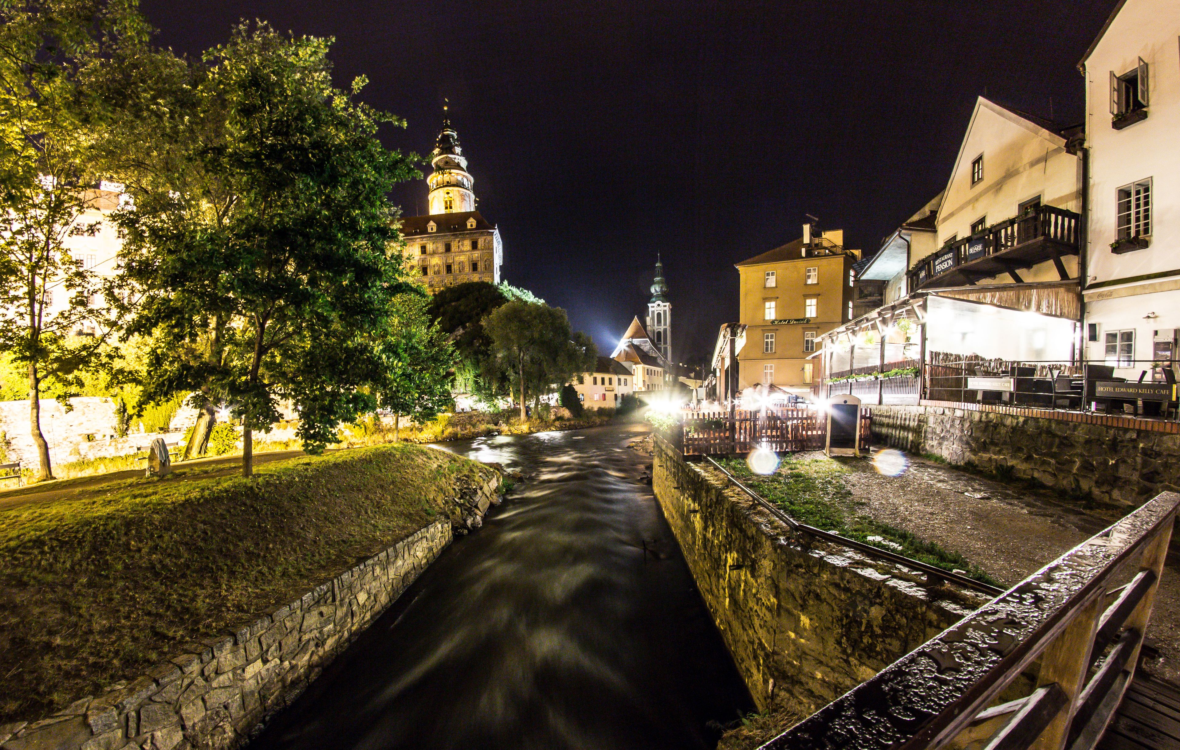 Une vue nocturne d’une rivière, avec des bâtiments de chaque côté, dont une tour imposante et un bâtiment doté d’un balcon.