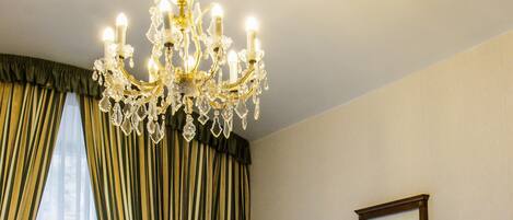 A hotel room with a large bed, a chandelier, a framed picture on the wall, and curtains on the window.