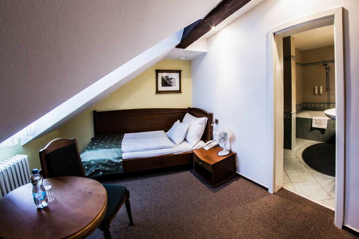 A bedroom with a bed, bedside table, and a small table with a bottle and glass.