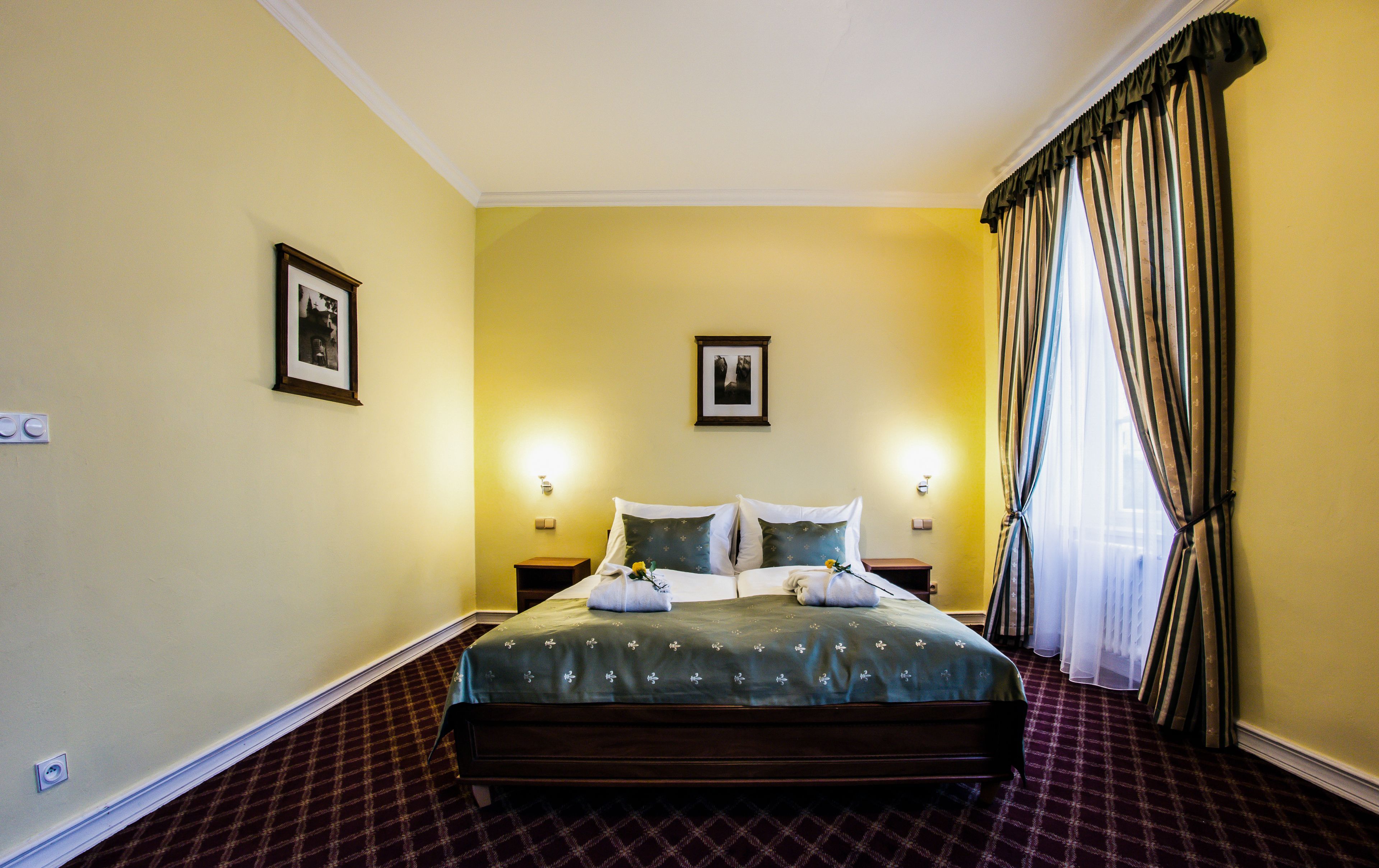 Habitación de hotel con una cama grande, dos mesitas de noche, una lámpara de pared y un ventanal con cortinas.