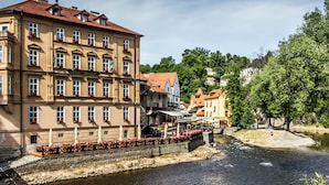 A riverside hotel with multiple floors, outdoor seating along the river, and a stone wall separating the riverbank from the building. - Hotel Dvorak (Cesky Krumlov)