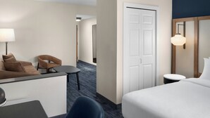 Habitación de hotel con cama, escritorio con lámpara, dos sillas, una mesita y una puerta.