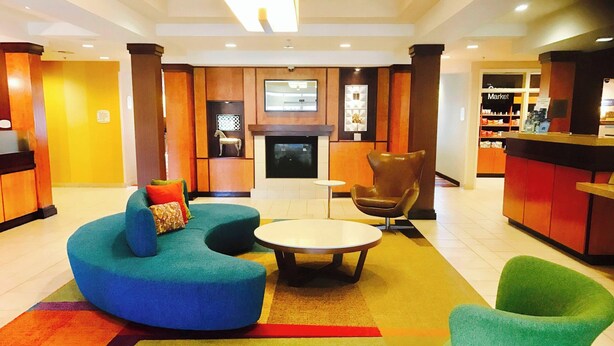 Un hall de hotel con una zona de estar que incluye una mesa redonda y dos sillones, una chimenea y un televisor montado en la pared.