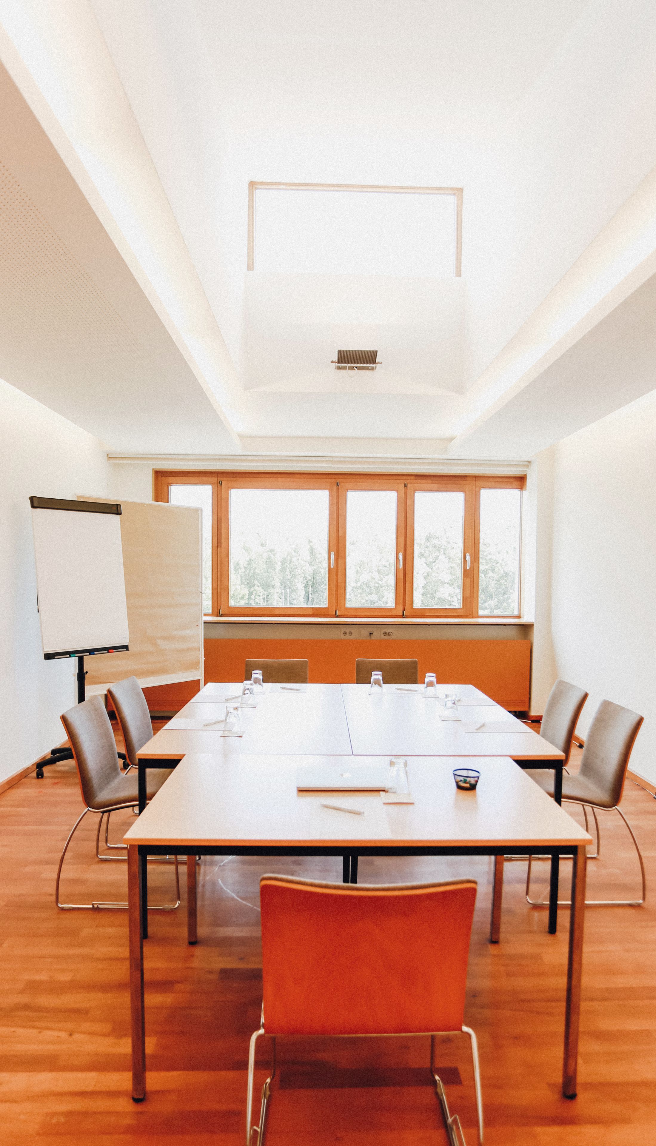 Ein Konferenzraum mit einem langen Tisch, sechs Stühlen, einer Whiteboard-Tafel und großen Fenstern.