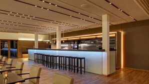 A modern bar area with a long counter and stools, surrounded by tables and chairs. - Ostseehotel Dierhagen (Ostseebad Dierhagen)