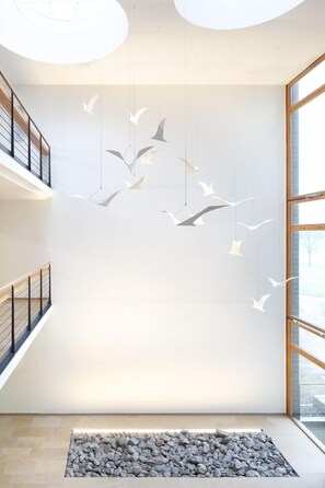 A modern interior with a hanging light installation, a stone feature at the bottom, and a view through large windows.