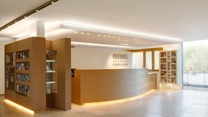 A hotel reception area with a wooden reception desk, a glass display case, and a large window offering a view of the outdoors. - Ostseehotel Dierhagen (Ostseebad Dierhagen)