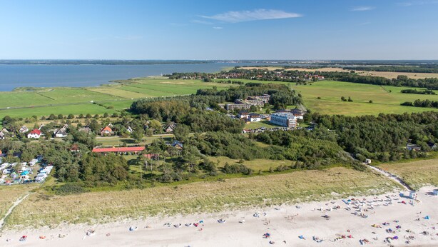 An aerial view of a coastal area with a beach, a large building complex, and surrounding fields. - Ostseehotel Dierhagen (Ostseebad Dierhagen)
