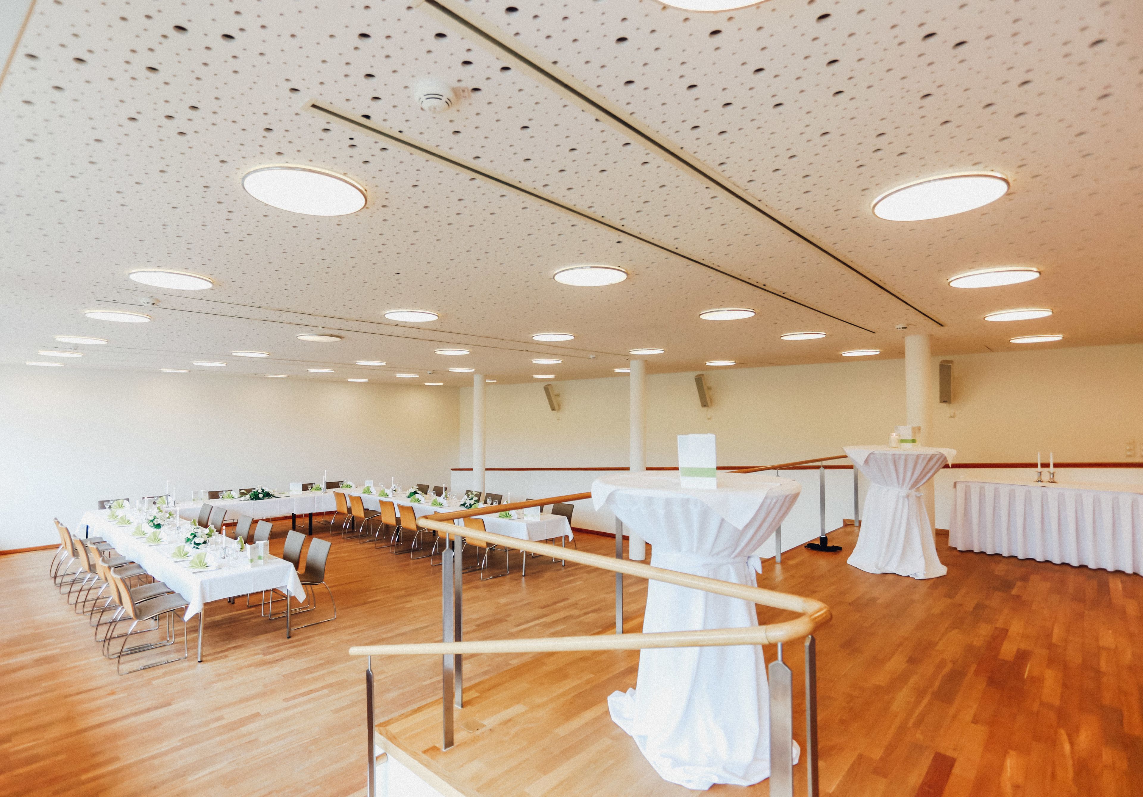 Une grande salle dotée de parquets en bois, de tables blanches et de chaises disposées pour un événement.