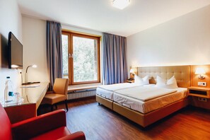 A hotel room with a bed, a desk, a chair, a TV, and a window with curtains. - Ostseehotel Dierhagen (Ostseebad Dierhagen)