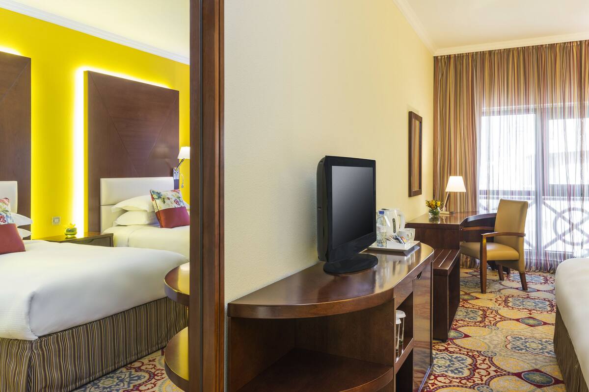 Une chambre d’hôtel comprenant un lit, un bureau avec un téléviseur à écran plat, une chaise et une fenêtre avec des rideaux.