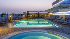 Un área de piscina en la azotea con sillones de descanso, un jacuzzi y una zona de estar cubierta.