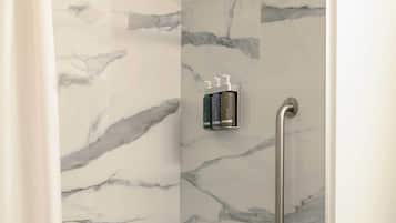 A modern bathroom with a marble wall, a bathtub, a shower with a handheld showerhead, and a grab bar.
