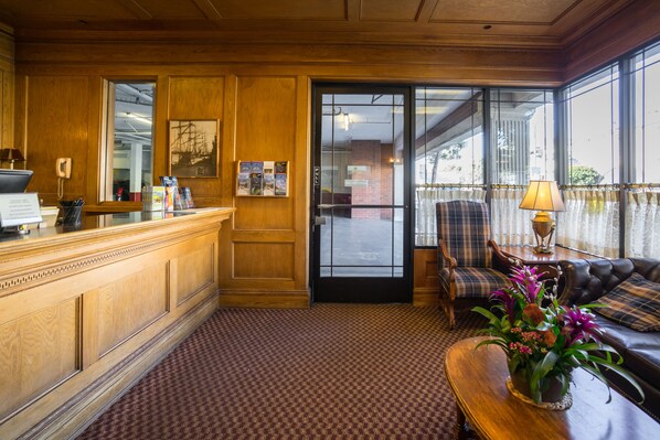 A reception area with a wooden reception desk, a seating area with a sofa and armchairs, and a window with a view of the outside.