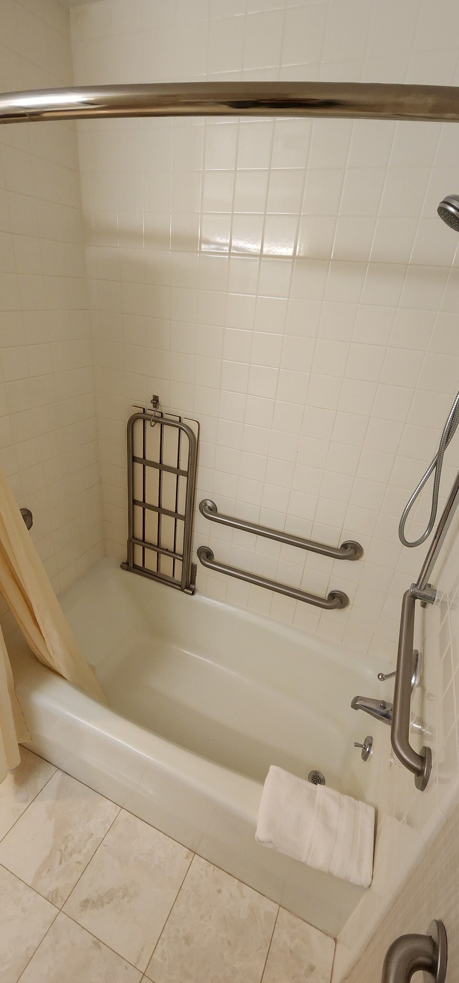A bathroom with a bathtub, grab bars, a showerhead, and a towel rack.