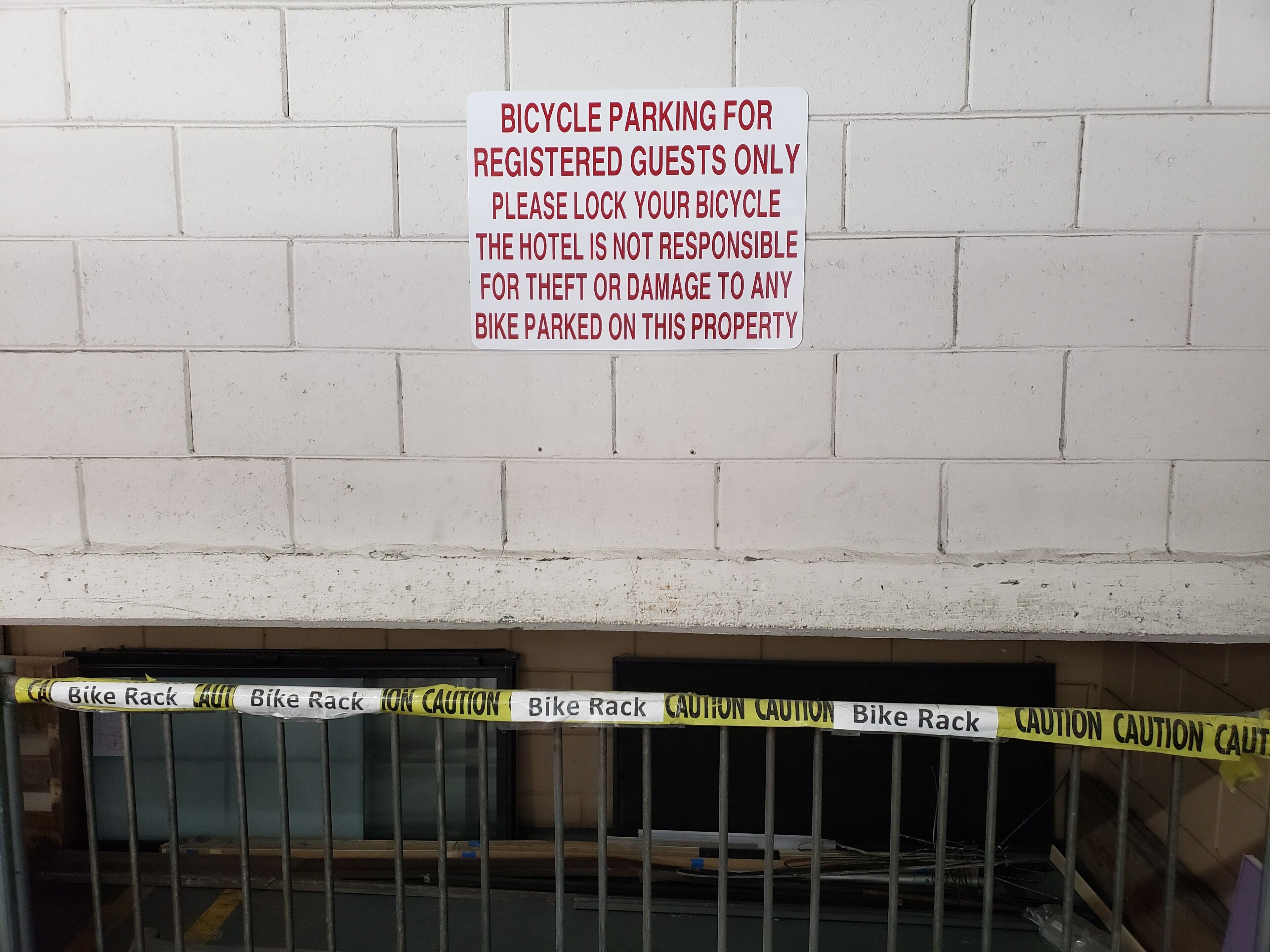 A sign indicating bicycle parking for registered guests only, with a caution tape warning about bike rack safety.
