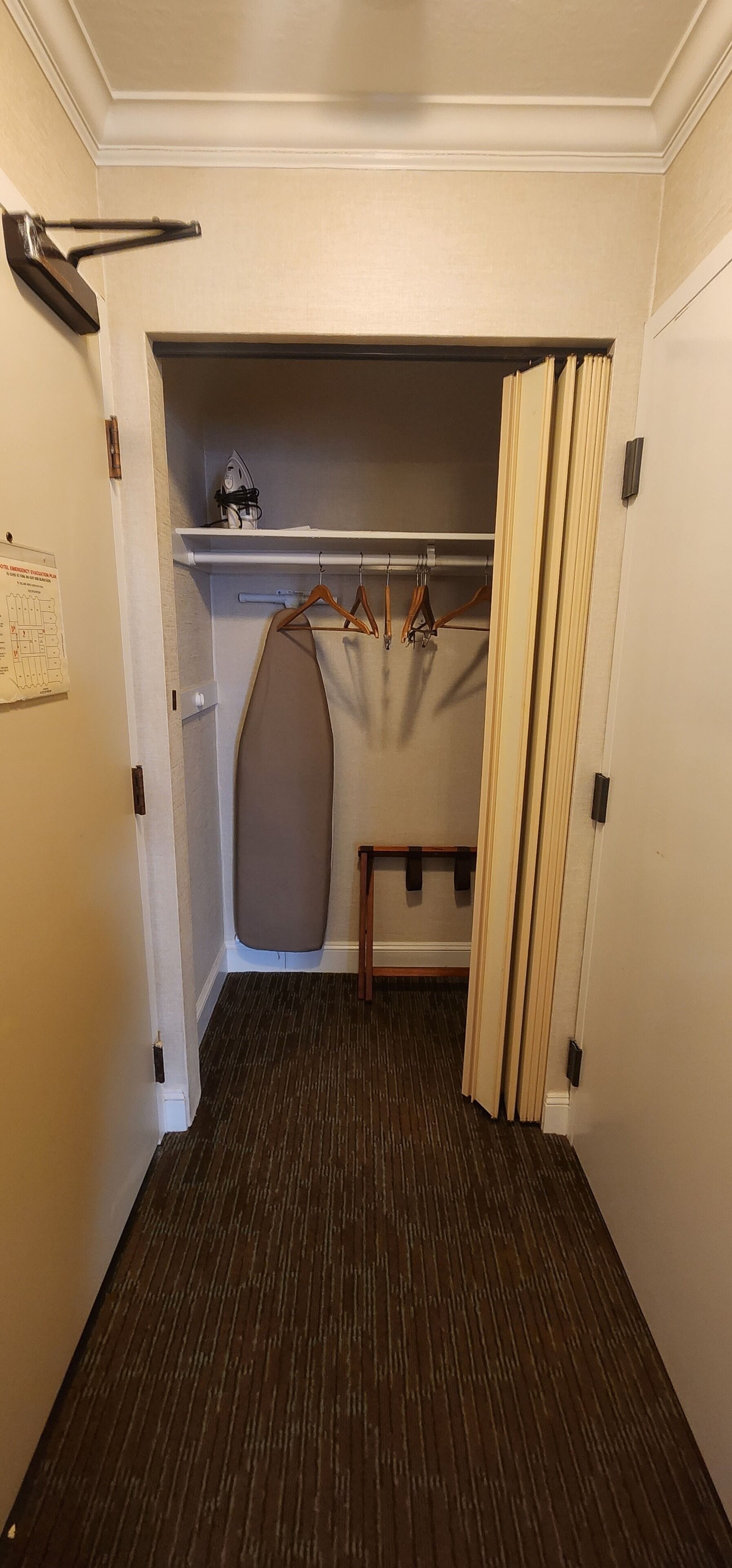 A narrow hallway with a wooden floor, a closet with hanging clothes, and a ceiling-mounted iron.