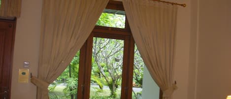 A room with a large window, curtains, a bed, and a chair.