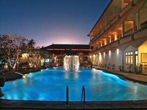 A swimming pool with a waterfall feature, surrounded by a building with multiple balconies and potted plants. - Febri's Hotel & Spa (Kuta)