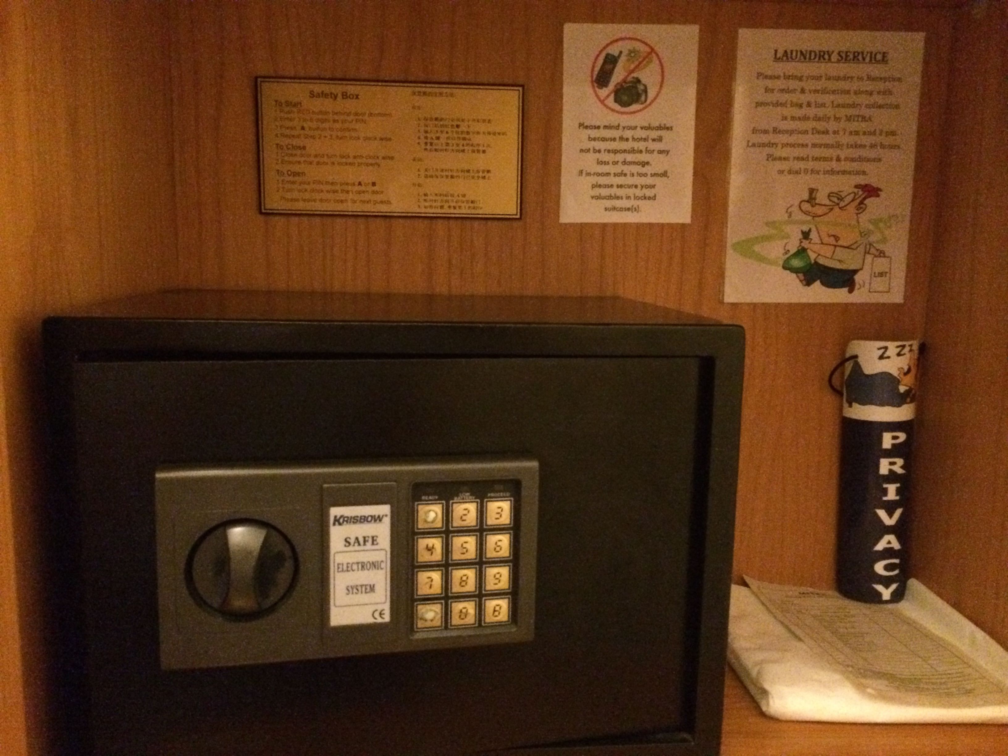 Ein Tresorraum mit Zahlenschloss, einem Sicherheitsschild und einem Hinweis zum Wäscheservice an der Wand.