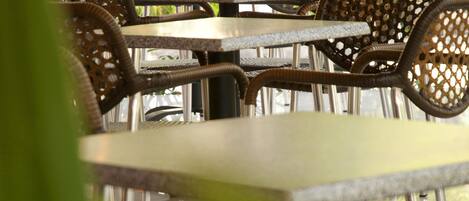 Outdoor seating with wicker chairs and metal tables, surrounded by greenery and trees.