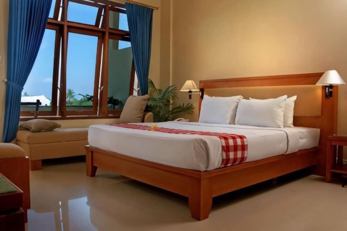 A hotel room with a bed, a sofa, a nightstand, a lamp, and a window with curtains.