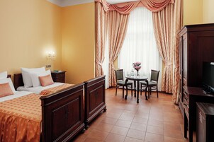 Quarto de hotel com duas camas, uma mesa de jantar com cadeiras, televisão e janela com cortinas.