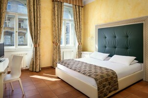 Quarto de hotel com uma cama, uma escrivaninha e uma cadeira.